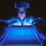 Investigadora trabajando con gel de electroforesis bajo luz ultravioleta en laboratorio biomolecular