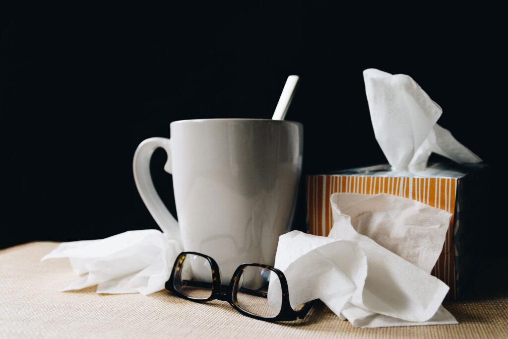 Taza de bebida caliente junto a pañuelos y gafas, símbolo de resfriado o cuidado en casa