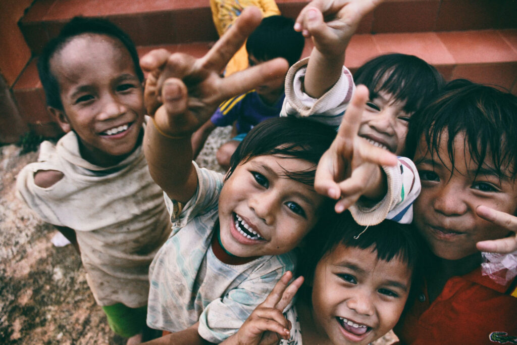 Grupo de niños sonrientes haciendo la señal de la paz mientras miran a la cámara.