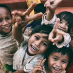 Grupo de niños sonrientes haciendo la señal de la paz mientras miran a la cámara.