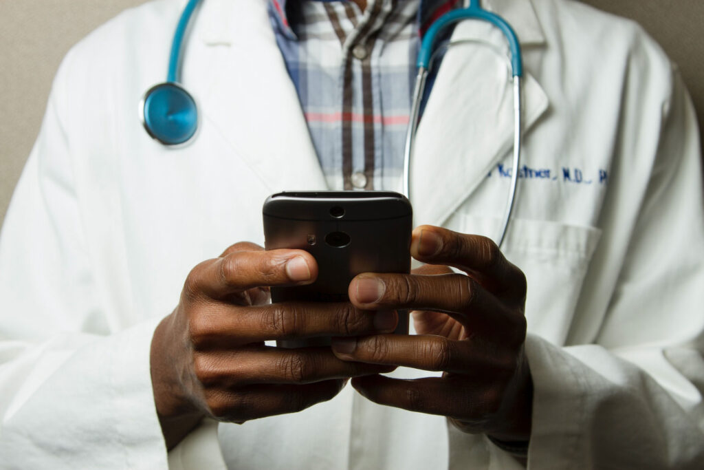 Médico revisando su teléfono móvil con un estetoscopio azul colgado del cuello.