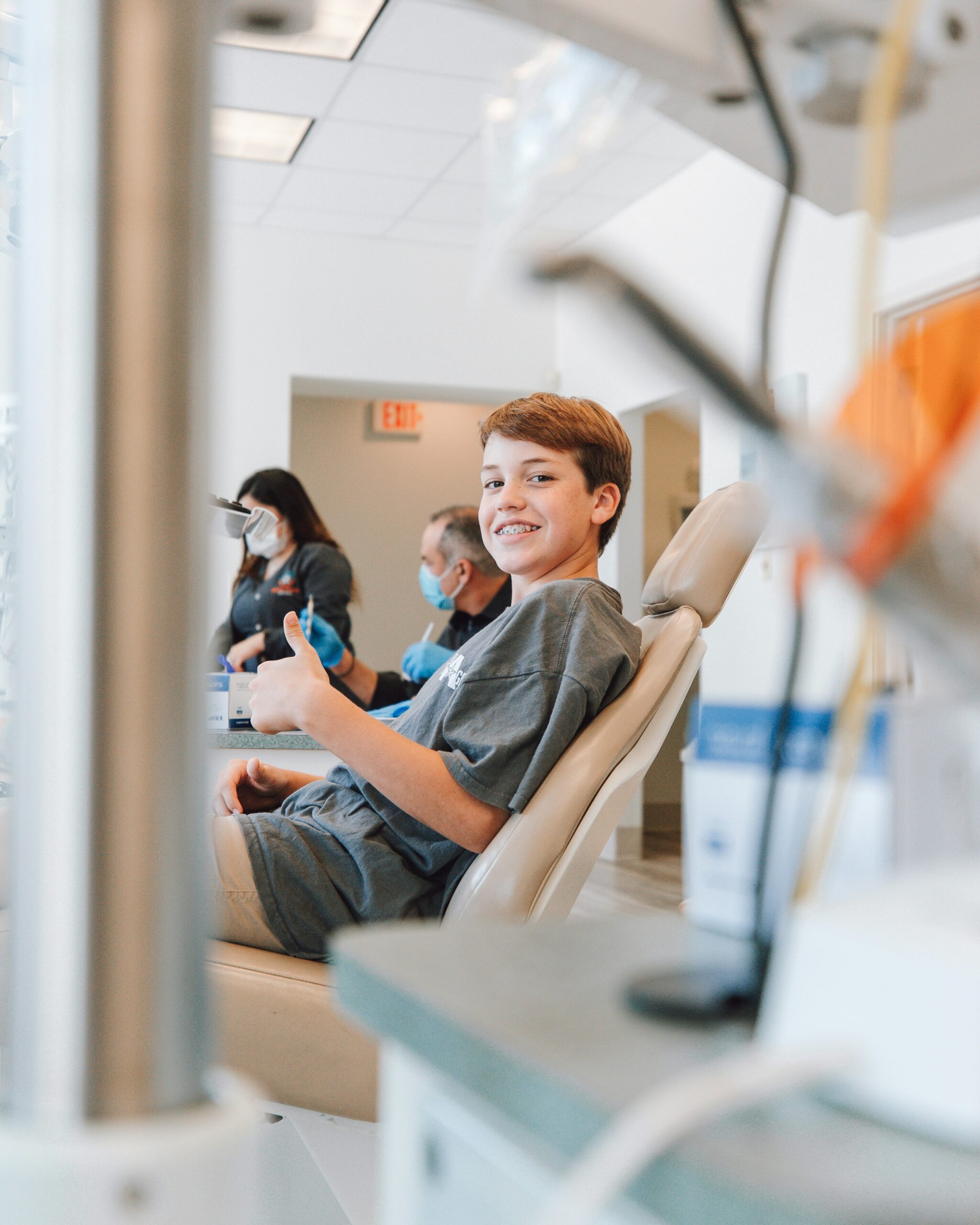 Niño con brackets sonriendo y levantando el pulgar en una clínica dental